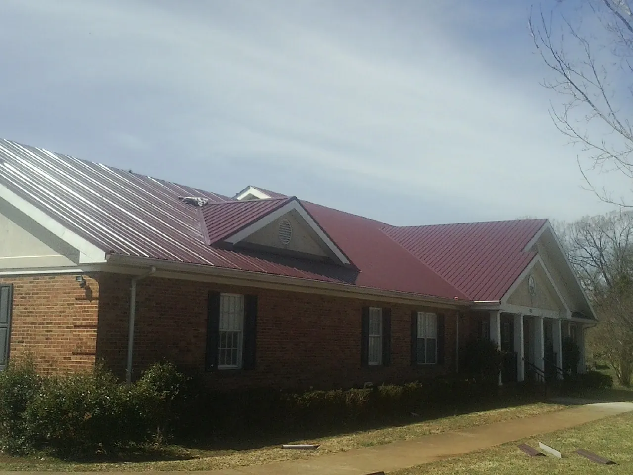 Red metal roof with gabled entries on a long brick building, from a Hail Damage Roof Repair job in Burnside