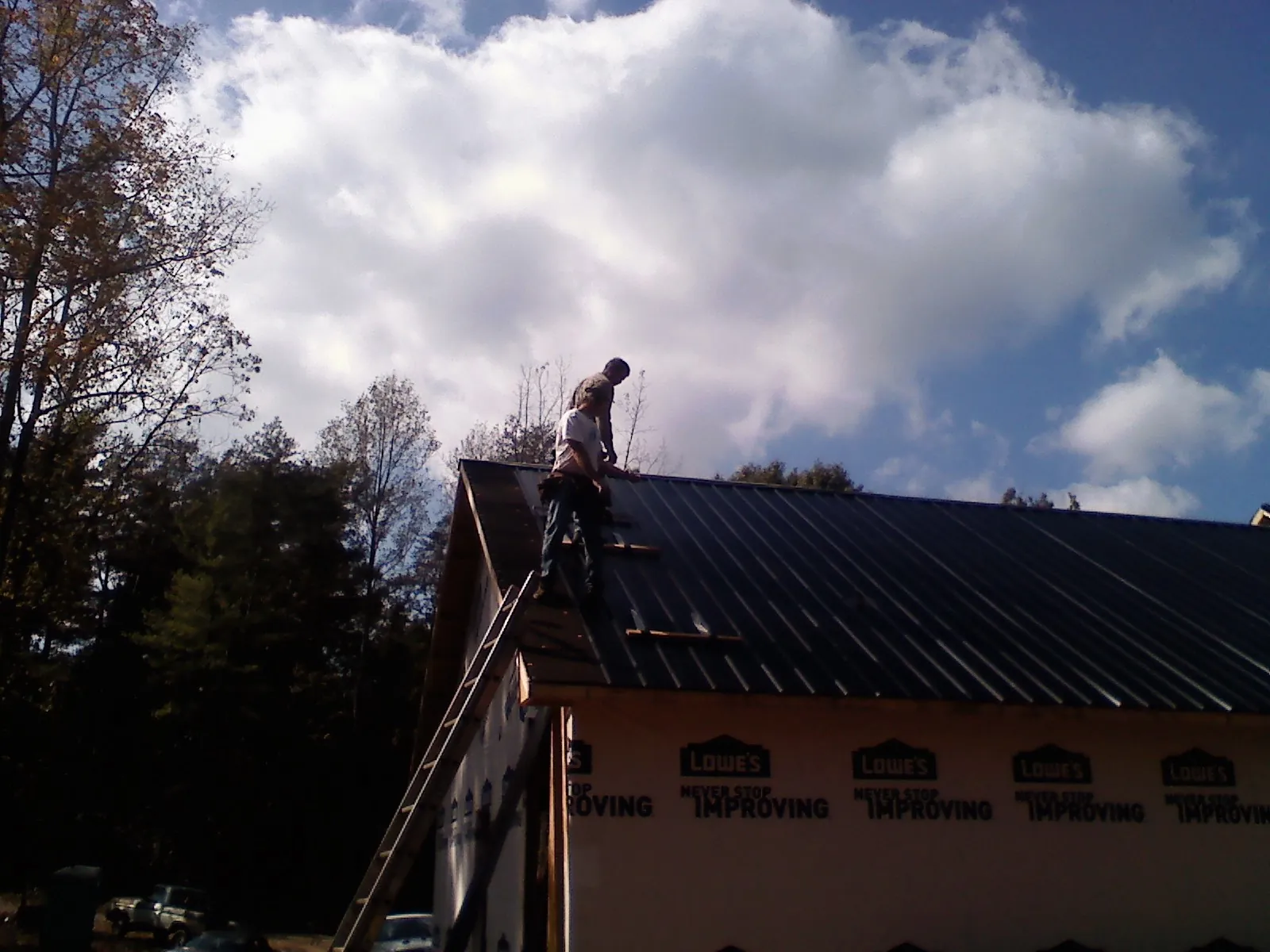 Roofer fastening dark metal panels high against a cloudy sky, from a Roof Inspection job in Burnside
