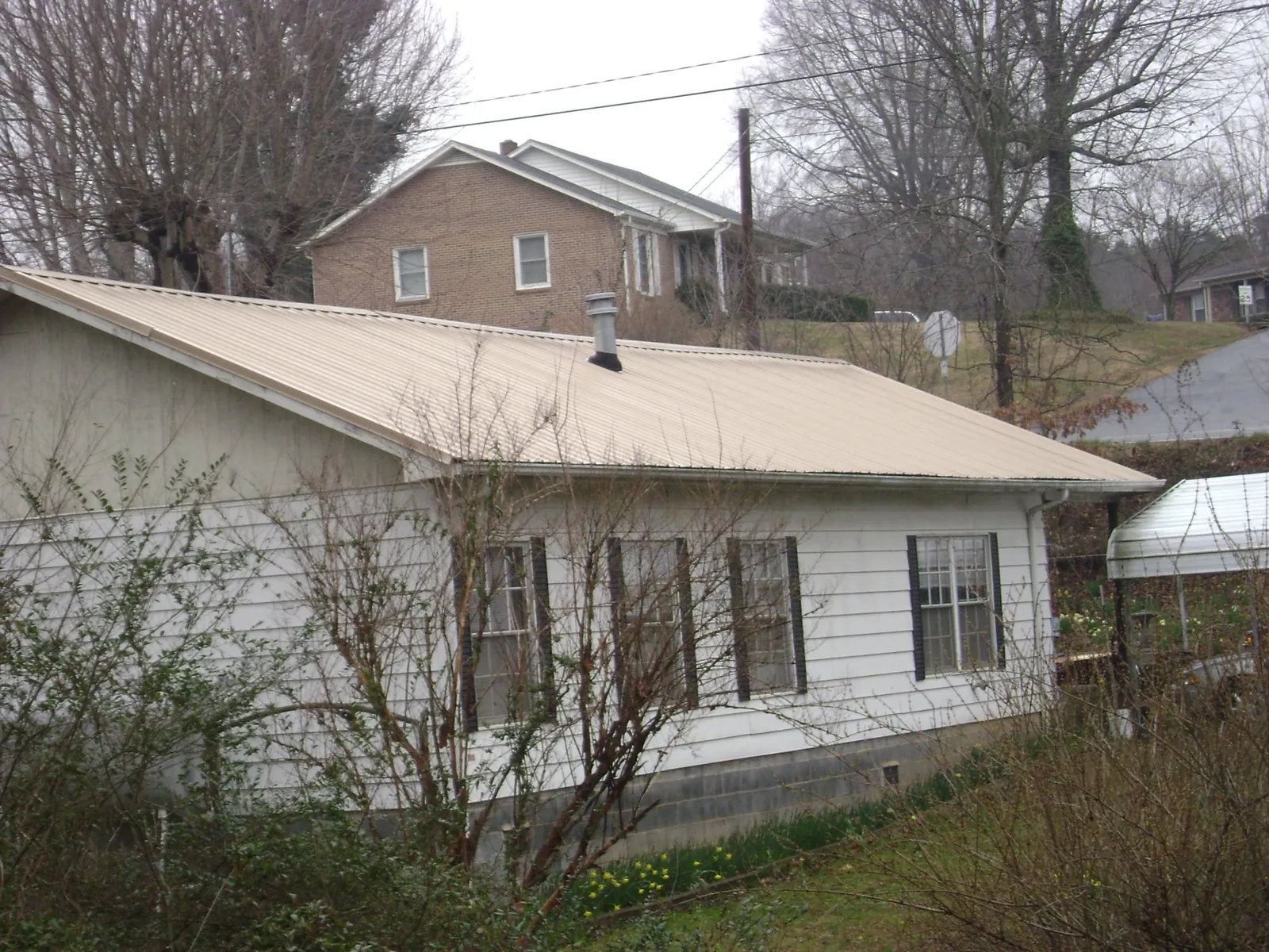 Tan metal roof on a white sided house set into a hillside — Commercial Roofing by Roofing Brothers in Burnside
