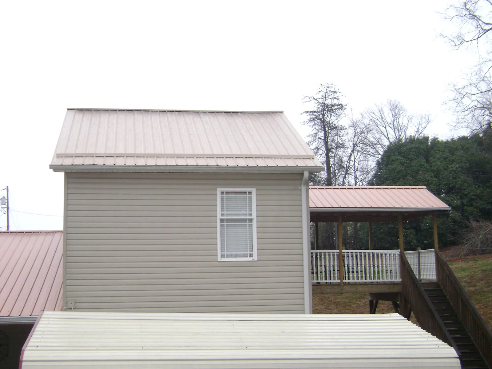 Tan metal roofs on a two story addition and attached porch, from a Roof Replacement job in Burnside