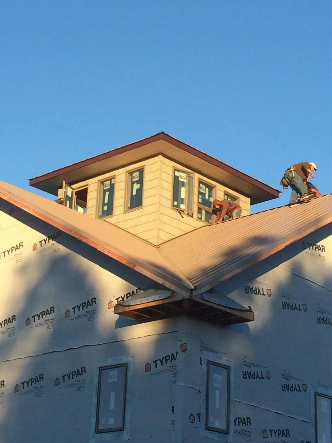 Roofers working around a rooftop cupola on a new metal roof at sunset in Burnside